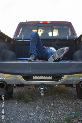 Casual rural lifestyle shot of a person resting in the bed of a red pickup truck. Represents freedom, relaxation, country living, and outdoor adventures.