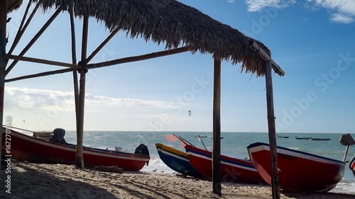 Kitesurfers sailing in the sea with fishing boats on the beach.