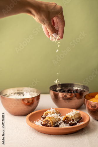 A hand sprinkling fresh coconut into a baklava dessert