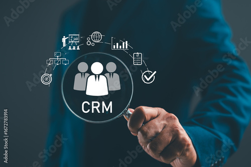 A person holding a magnifying glass over CRM icons, symbolizing customer relationship management and data analysis.