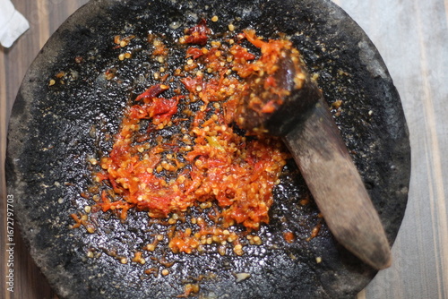 A close-up shot of freshly ground chili paste in a traditional stone mortar and pestle.