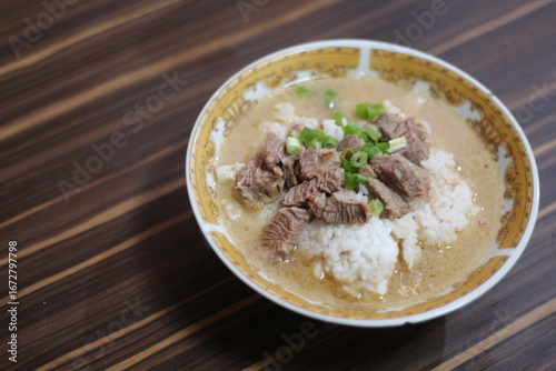 A close-up of a (coto makassar) delicious beef rice bowl with tender slices of beef, topped with fresh green onions, served in a flavorful broth.