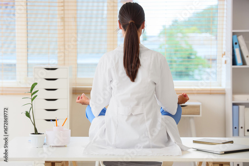 Female doctor meditating on table in clinic, back view