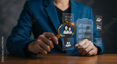 A person in a suit is using a magnifying glass to review potential candidates or employees, symbolizing human resources management.