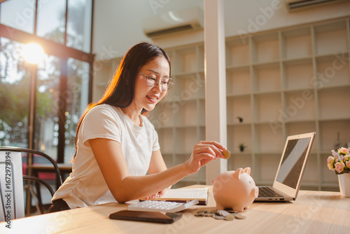 A young Asian woman saves money by putting coins in a pink piggy bank. The concept of saving money.