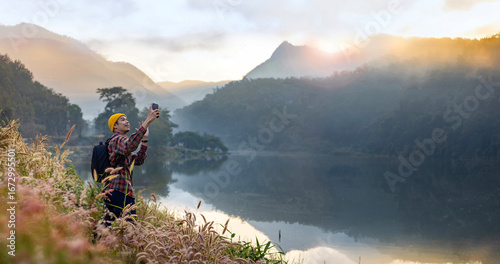Asian naturalist taking selfie photo using mobile phone while exploring wildlife in forest at lake for surveying and discovering rare biological diversity and ecologist on the field in autumn