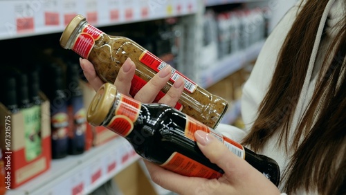 Photos Customer comparing two sauce bottles in a supermarket and making a decision base