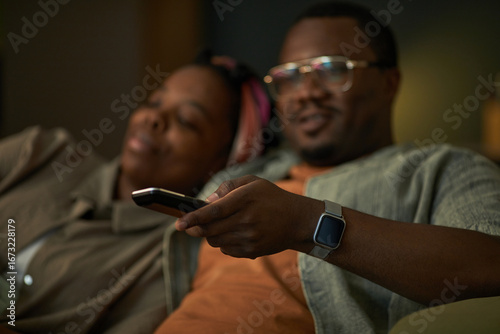 Canvas Print Black man holding remote control sitting next to Black woman relaxing on couch w