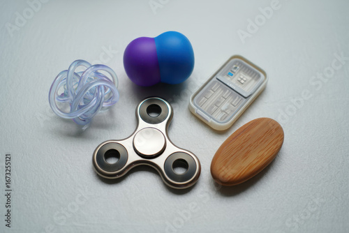 A collection of fidget toys including a spinner, stress ball, and a wooden oval object on a white surface