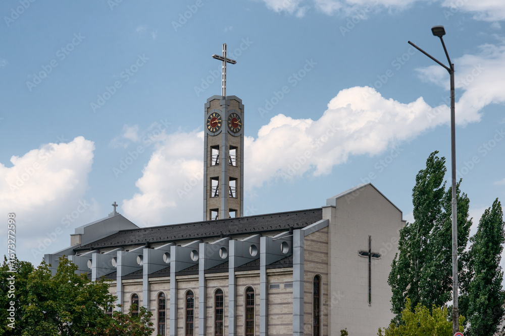Obraz premium Catholic Cathedral of St. Joseph Parish with modern architectural design, featuring its clock tower, cross, and facade details under a bright summer sky.