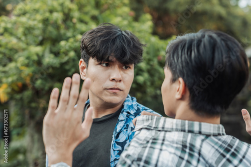 A larger Southeast Asian man glares menacingly at a smaller peer, who cowers under pressure with lowered gaze in a tense display of intimidation and dominance.