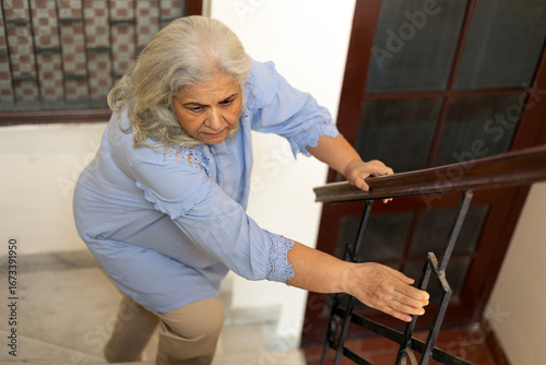 Indian elderly old woman walking up stairs in house. Asian aged woman went up stairs. Grandma home alone walking up stairs have pain knee ache in house