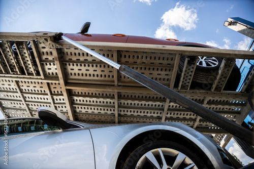 Bottom of pre-owned red SUV car on upper car hauler platform, silver wagon under, lifted on car carrier trailer, hauler, auto transport trailer, semi-trailer with hydraulic piston.