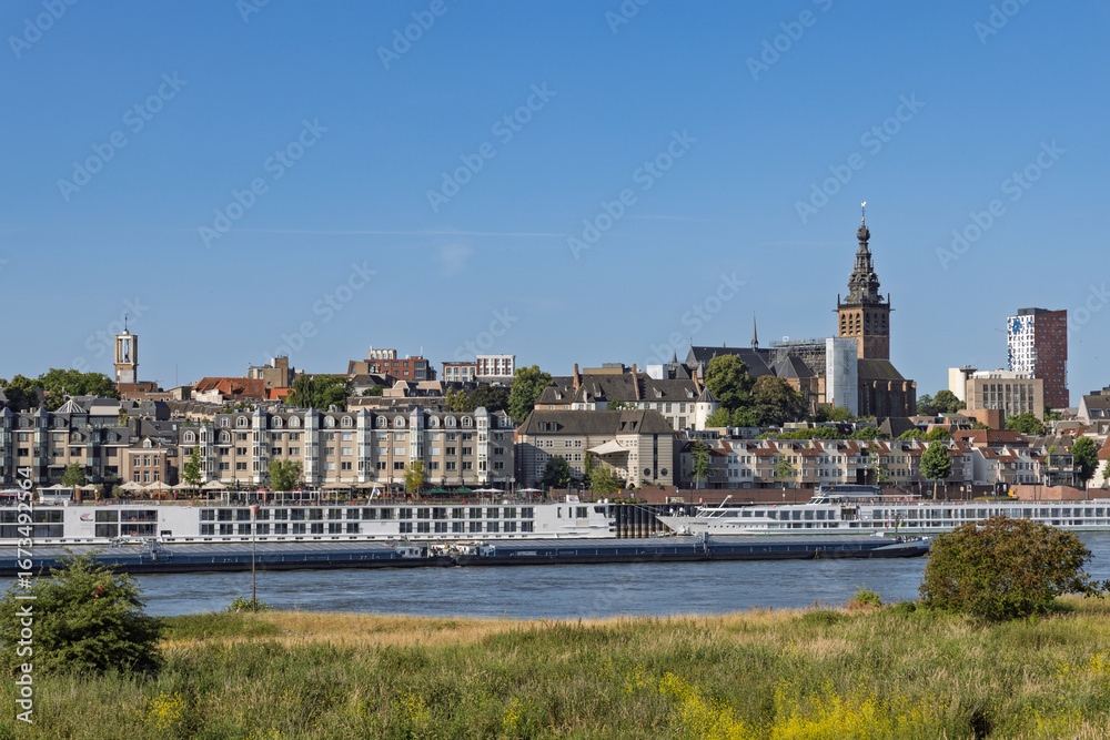 Fototapeta premium The cityscape of Nijmegen with a focus on the riverside buildings, the St. Stephen's Church, and cruise ships. Nijmegen, Netherlands. 20 June 2025.