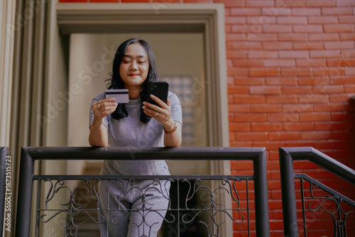 Asian young woman using smartphone, shopping online holding credit card and making payment at home. Web subscriptions e-commerce, checking electronic wallet balance, e-banking and online transactions.