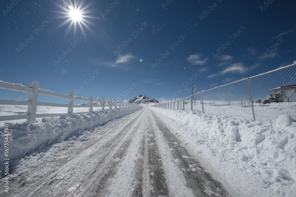 Obraz premium Snowy road leading to a mountain under a bright sun