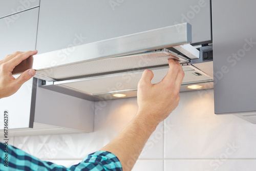 Mans hands removing a filter from cooker hood for cleaning or service. Replacing filter in kitchen hood. Modern kitchen fan or range hood.