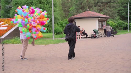 Colorful balloon vendor strolls through park as passersby enjoy sunny afternoon in vibrant outdoor setting