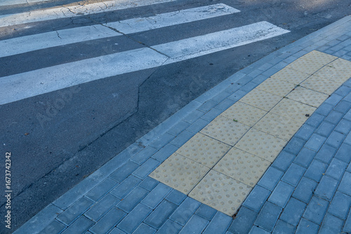 Fotografie A crosswalk is visible with marked white stripes on a city street, accompanied b