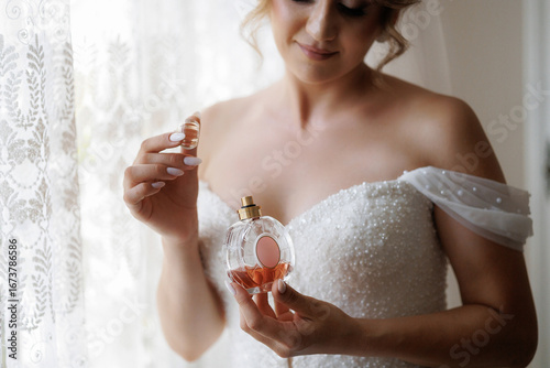 Fotografie Bride preparing for wedding day with perfume in elegant setting by window