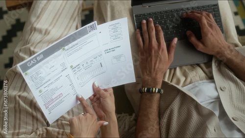 High angle cropped shot of hands of unrecognizable couple looking at utility bills and paying them online using laptop, managing home budget together