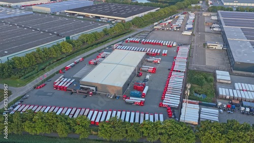 Aerial drone of transport hub and distribution warehouses with trucks at sunset