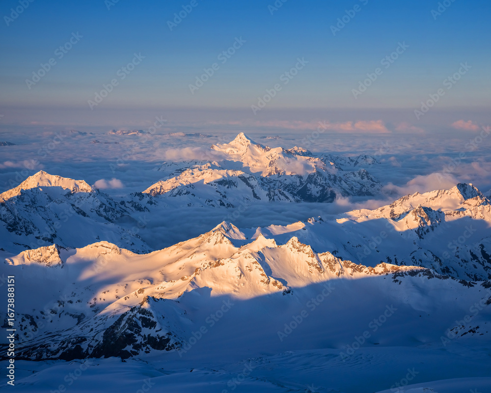 Obraz premium The first rays of the sun illuminate the mountains of the Main Caucasian range. View from Pastukhov cliffs on the Mt. Elbrus slope in Russia.