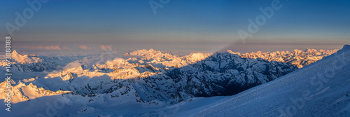 The first rays of the sun illuminate the mountains of the Main Caucasian range. View from the Mt. Elbrus slope in Russia.