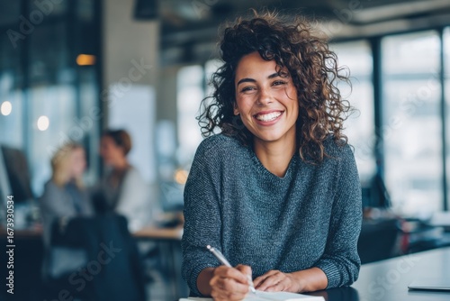 Happy smiling young woman with curly hair working in modern office environment.