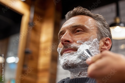 Mature man getting a traditional wet shave with a safety razor at barbershop.