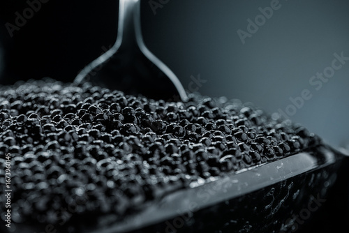 Delicious black caviar is being carefully scooped from a sleek container, showcasing its rich texture and color. The scene highlights the luxury of fine dining and gourmet cuisine.