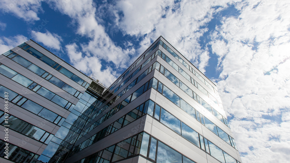 Fototapeta premium Modern Business. A low angle shot of a modern glass office building against a blue sky with the reflection of the sky and clouds in the building’s windows.