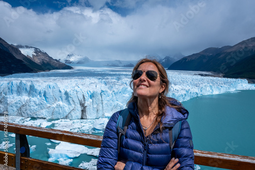 Smiling woman in sunglasses and winter jacket enjoying the breathtaking view of the Perito Moreno Glacier in Patagonia, Argentina