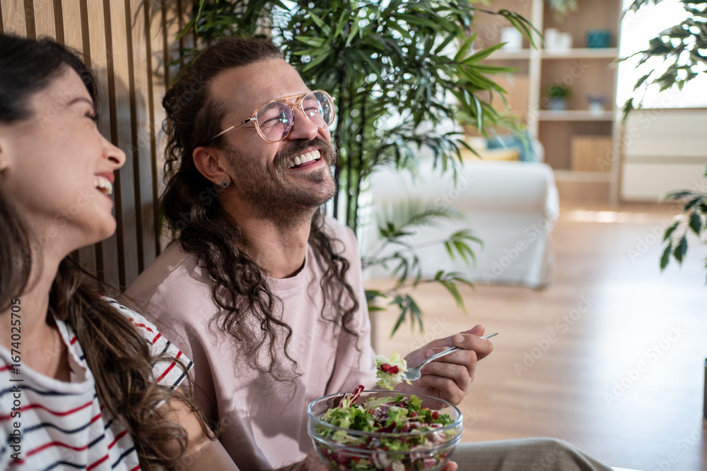 Obraz premium Couple laughing and eating salad at home