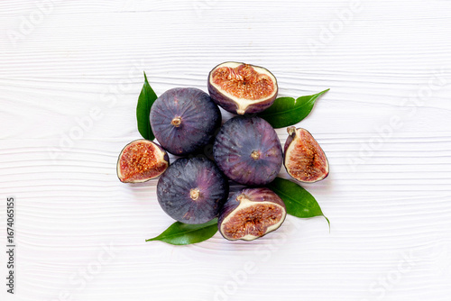 Purple ripe figs fruit and slices with green leaves top view on a wooden background