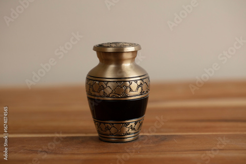 Valokuva A small, gold and black urn with an ornate pattern is displayed on a wooden surf