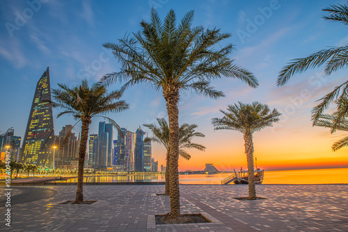 Doha city business downtown center panorama illuminated at sunrise, with modern skyscrapers and sea in the foreground, Qatar