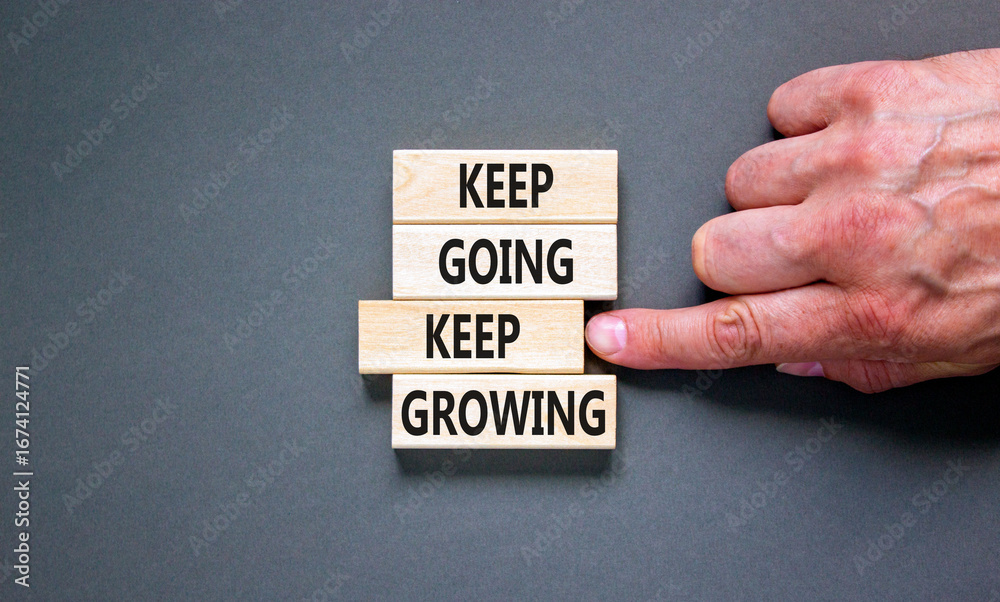 Keep going and growing symbol. Concept words phrase Keep going keep growing on beautiful wooden blocks. Beautiful grey background. Businessman's hand. Business Keep going growing concept. Copy space. Keep going and growing symbol. Concept words phrase Keep going keep growing on beautiful wooden blocks. Beautiful grey background. Businessman's hand. Business Keep going growing concept. Copy space.