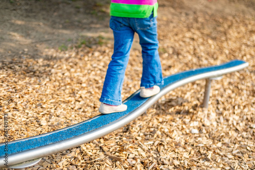 Quadro su tela Child walking balance beam in park, Little girl balancing outdoor equipment, gre