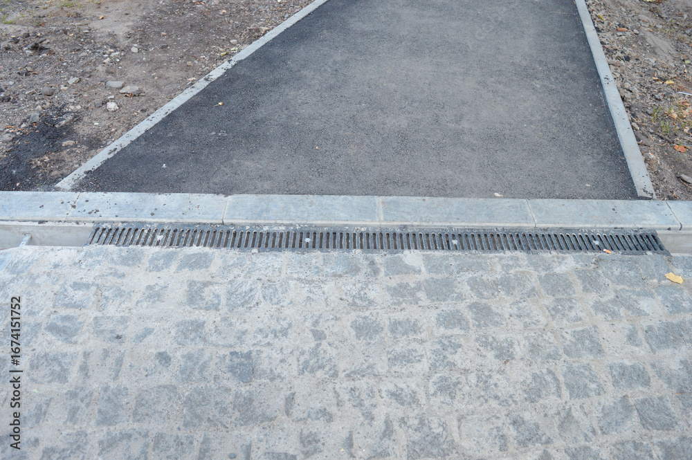 Fototapeta premium Overhead view of a transition between asphalt, stone pavement, and concrete curbing with a drainage channel. Concept for urban planning, road construction, and municipal infrastructure