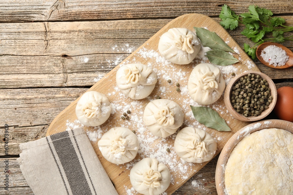 Fototapeta premium Uncooked khinkalis (dumplings) with peppercorns, flour, parsley and bay leaves on wooden table, flat lay