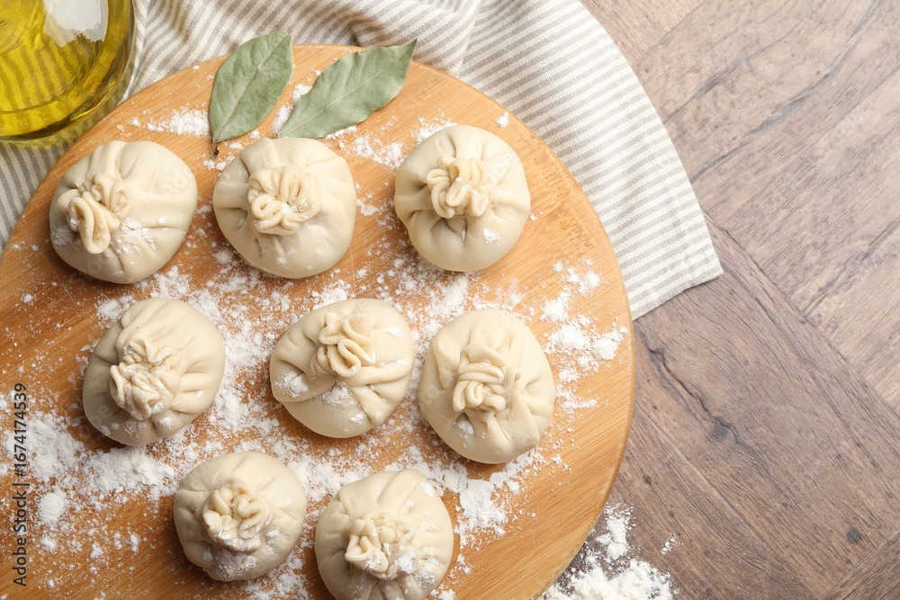 Fototapeta premium Uncooked khinkalis (dumplings) with flour, oil and bay leaves on wooden table, top view. Space for text