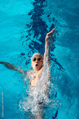 Swimmer boy swims backstroke swimming style in the pool
