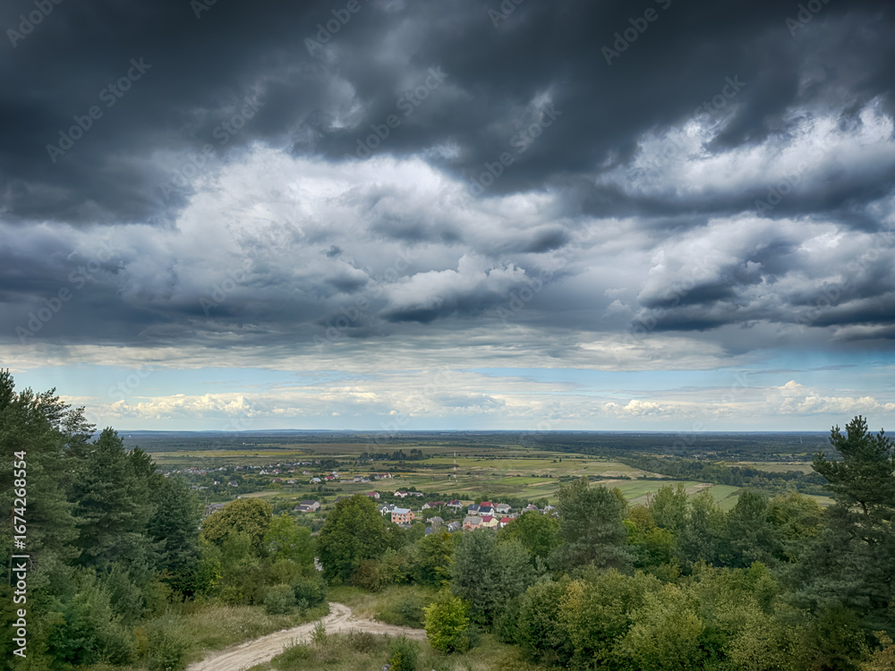 Fototapeta premium Hilltop view of village under dramatic cloudy sky. Scenic panorama of countryside village before the rain