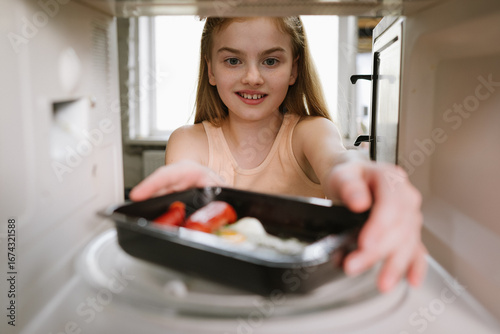 Behang Smiling girl putting ready meal tray into microwave oven, view from inside the appliance