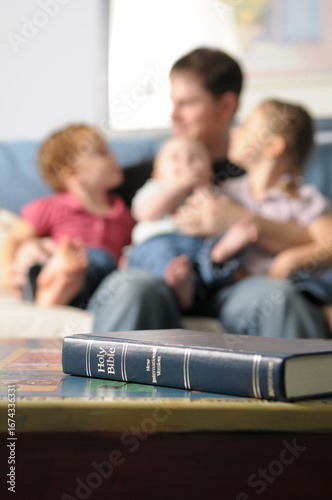 Bible on Table with Father and Children on Couch in Background