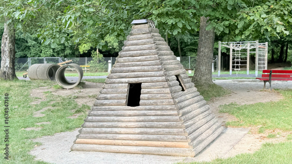Obraz premium Wooden pyramid hut in playground, outdoor eco playhouse for children, rustic wooden structure for kids fun and recreation, natural park equipment for family leisure activities. High quality photo