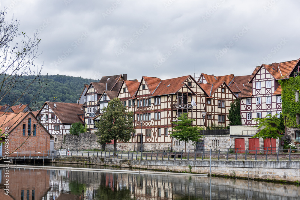 Fototapeta premium Historic German architecture with half timbered buildings, riverside reflections, and cloudy sky background