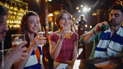 Sport fans clinking beer watching television in dark bar closeup. Smiling people