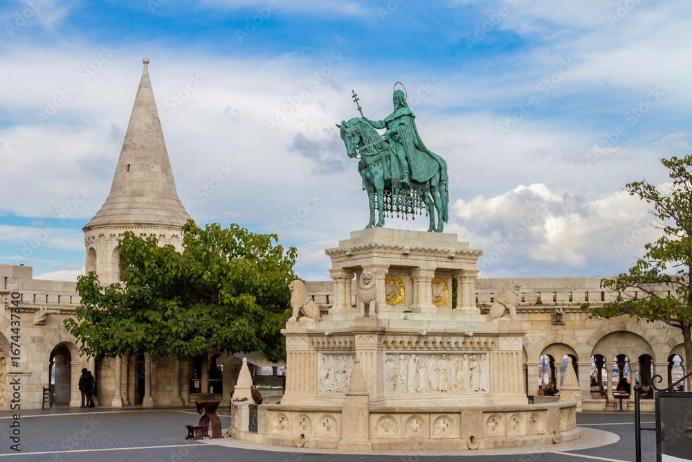 Obraz premium Impressive bronze equestrian statue of King Saint Stephen against Fisherman's Bastion arches and towers under sunny blue sky. Budapest, Hungary.